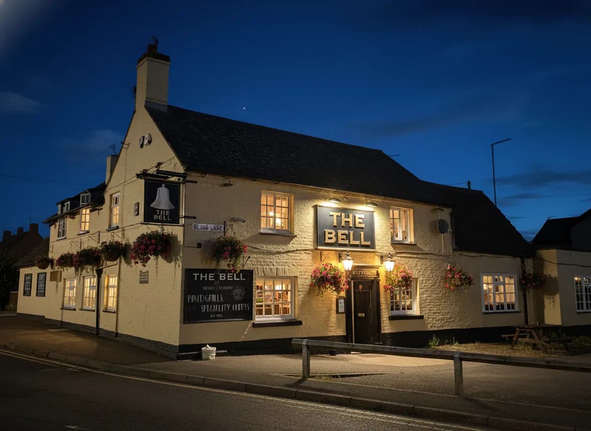 The Bell Sawtry exterior at night with lanterns, fire pits, and glowing windows.