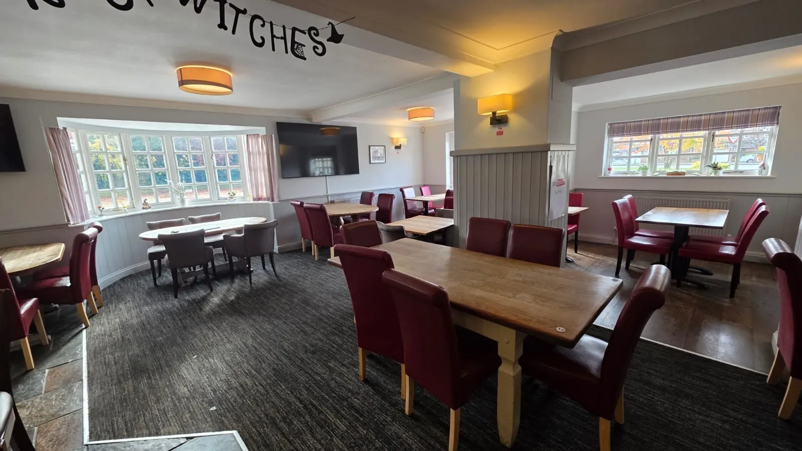 Second dining room with wooden tables, patterned chairs, and large windows.