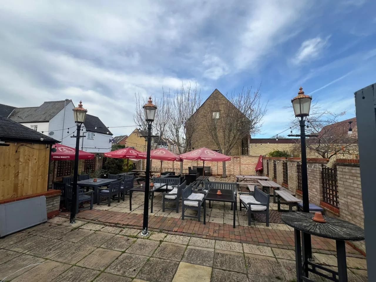 Panoramic beer garden along the river with deck seating, planters, and festoon lighting.