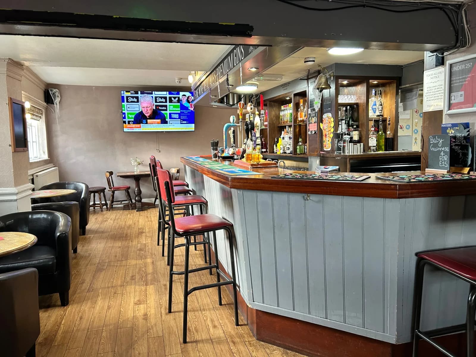 Bar area with timber counter, upholstered stools, and a backlit spirits display.