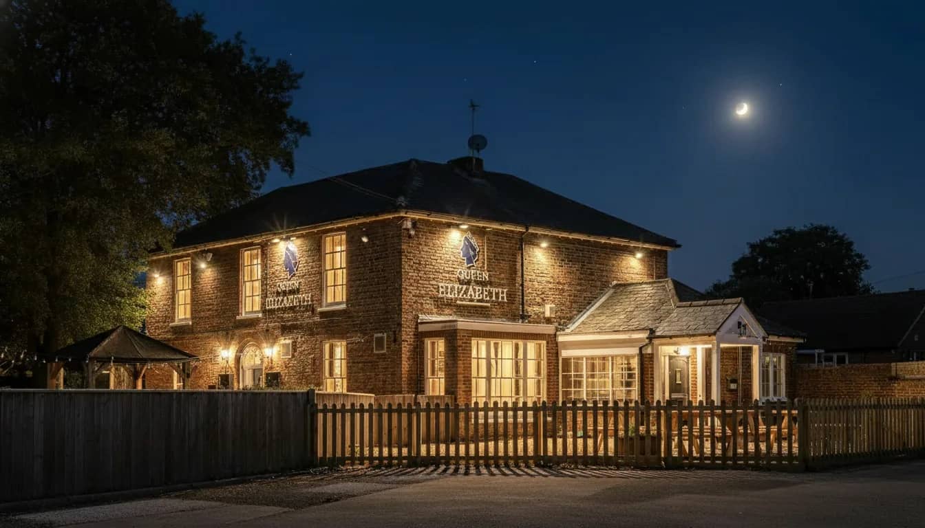 Queen Elizabeth pub exterior at dusk with lantern-lit benches facing Gayton Road.