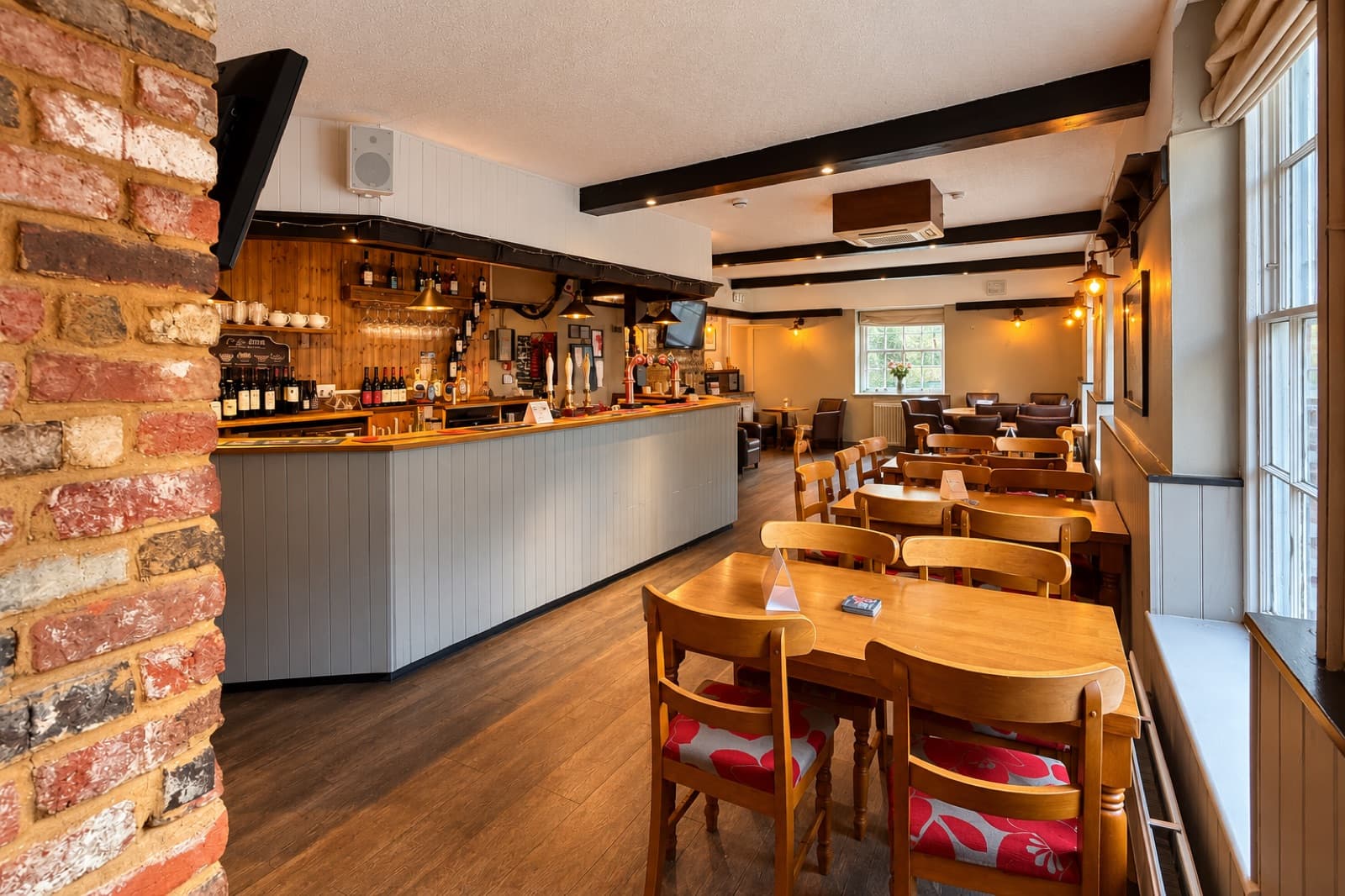 Grey-panelled bar on the left and wooden tables beside sash windows at The White Horse Inn in Swavesey.