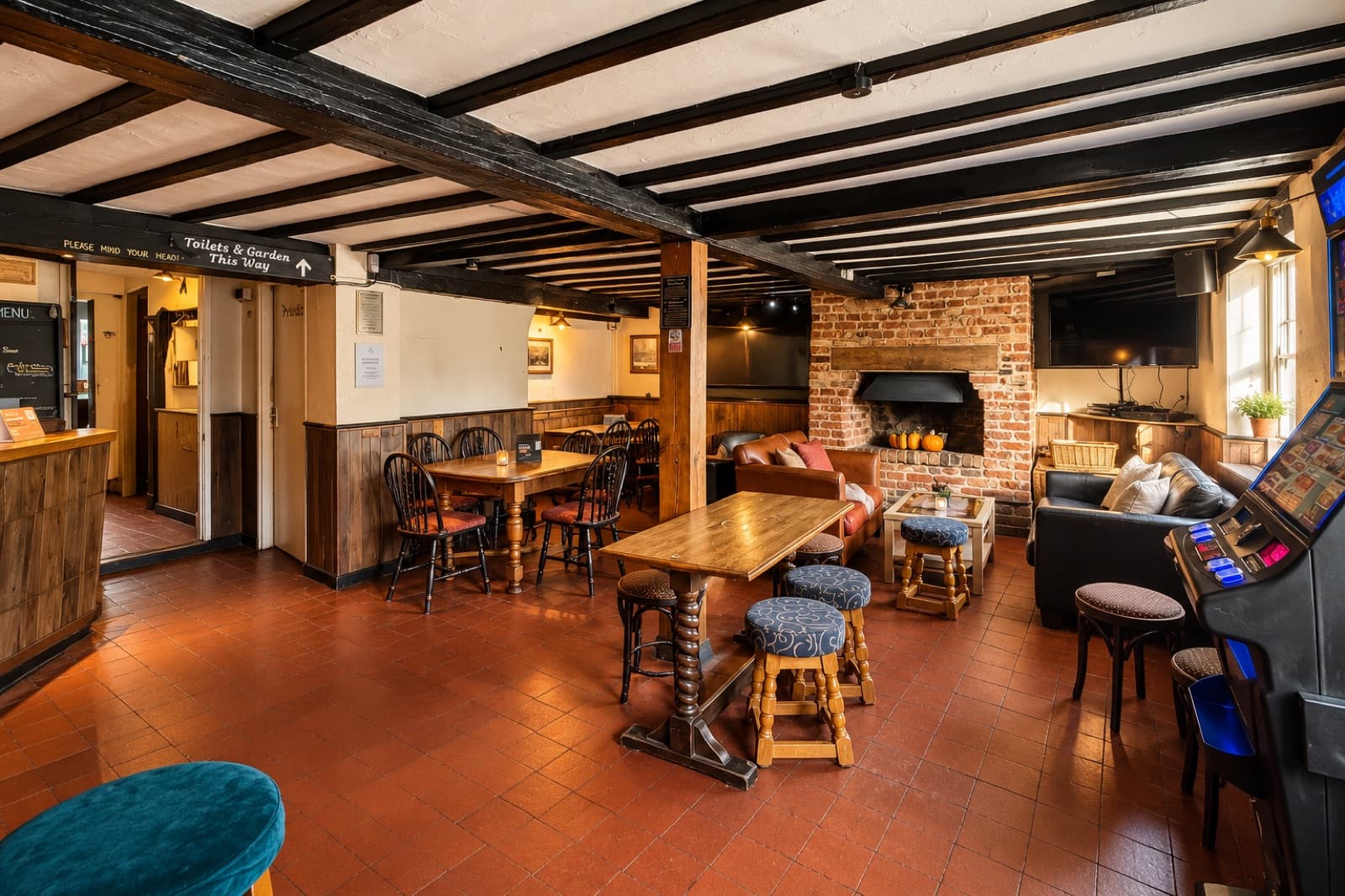 Black timber beams, a brick fireplace, sofas and wooden tables at The White Horse Inn in Swavesey.