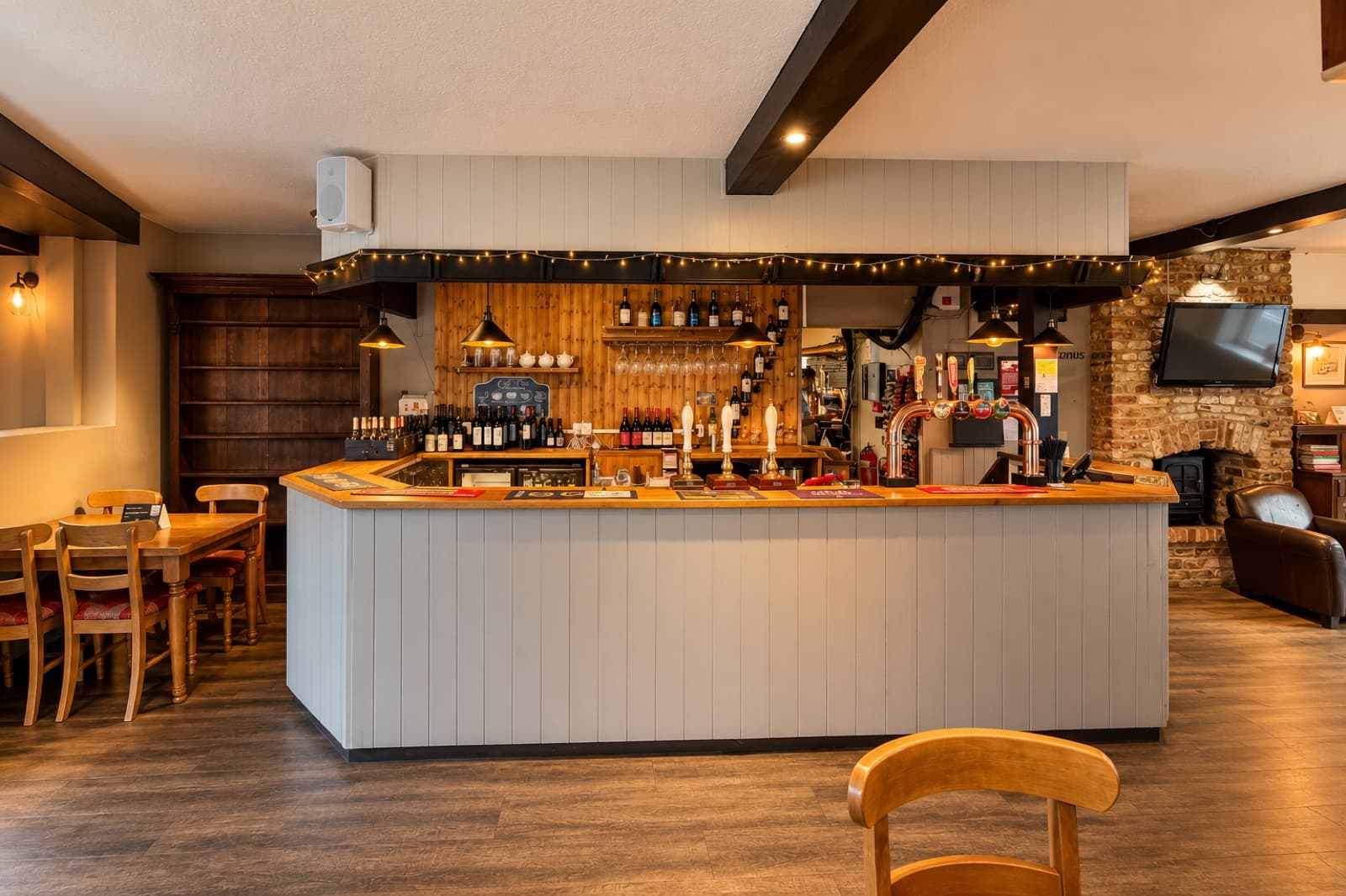 Grey-fronted bar with beer taps, hanging glasses and wooden shelves at The White Horse Inn in Swavesey.